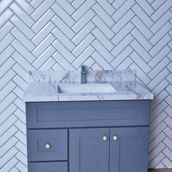 Gray bathroom vanity with marble countertop against herringbone tile wall.