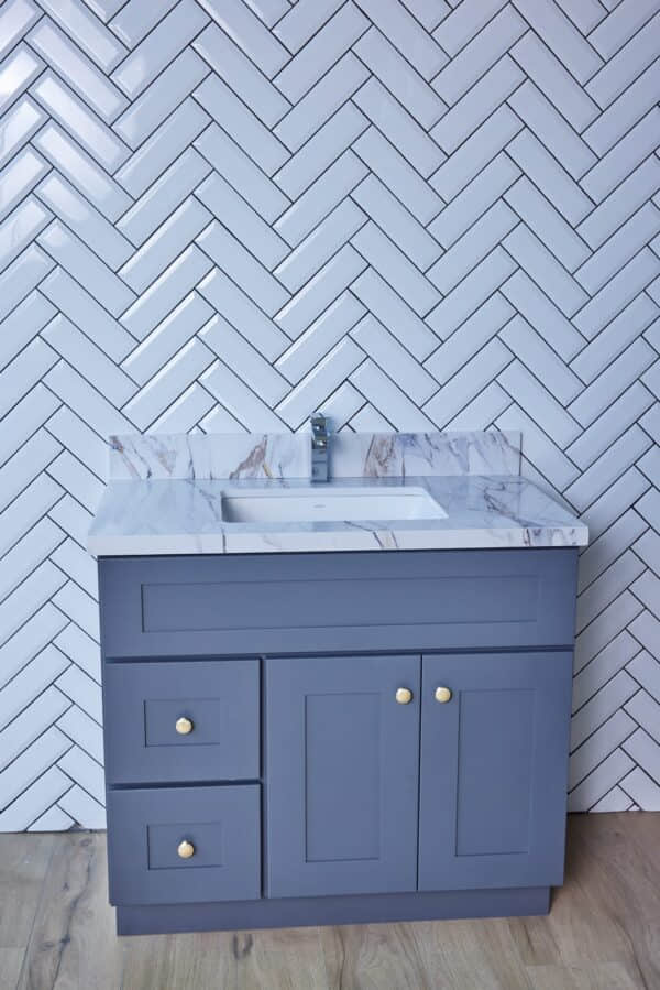 Gray bathroom vanity with marble countertop against herringbone tile wall.