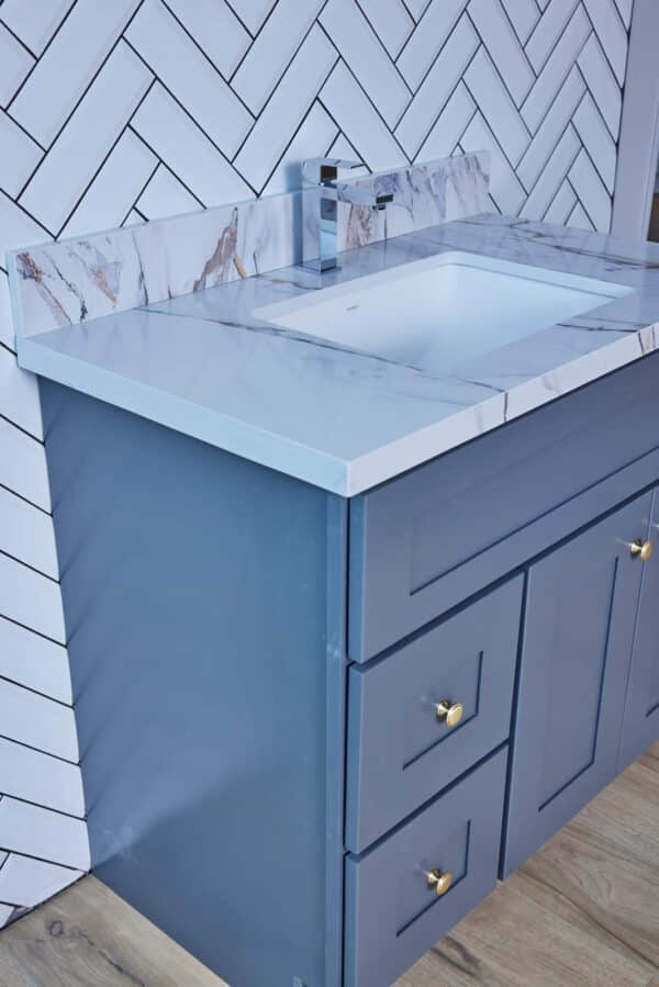 Blue bathroom vanity with marble countertop and herringbone tile backsplash.