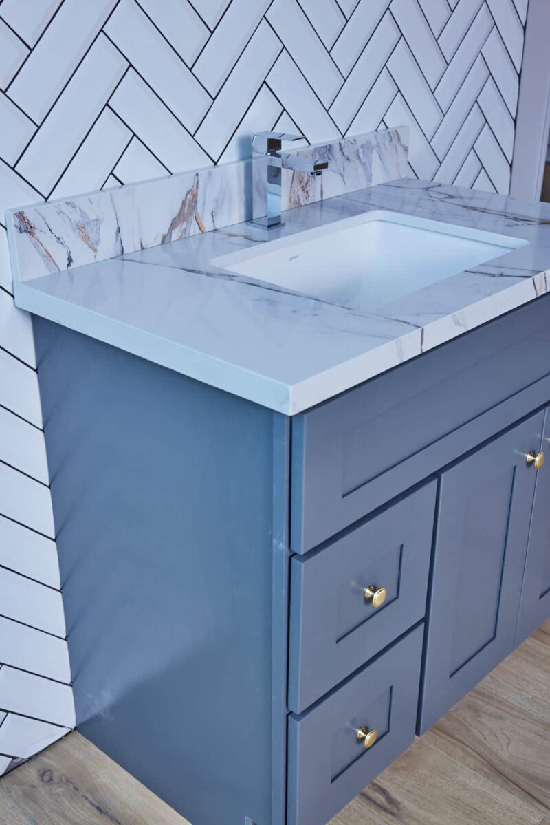 Blue bathroom vanity with marble countertop and herringbone tile backsplash.