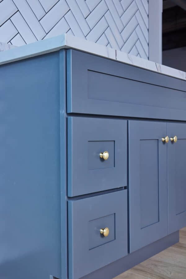 Blue kitchen cabinets with gold knobs and marble countertop.