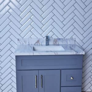 Gray bathroom vanity with marble countertop and herringbone tile backsplash.