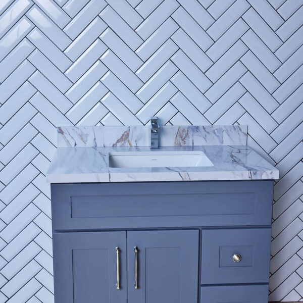 Gray bathroom vanity with marble countertop and herringbone tile backsplash.