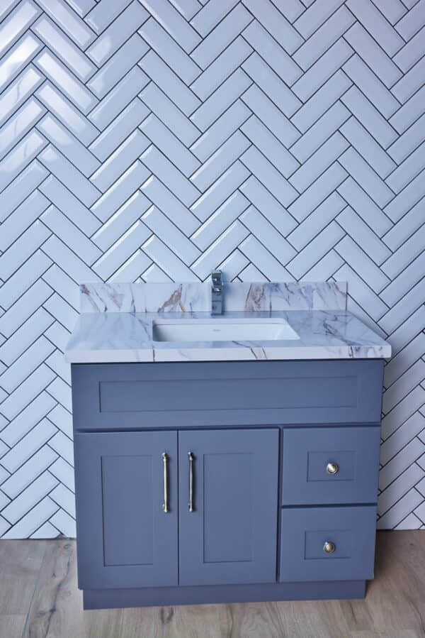Gray bathroom vanity with marble countertop and herringbone tile backsplash.