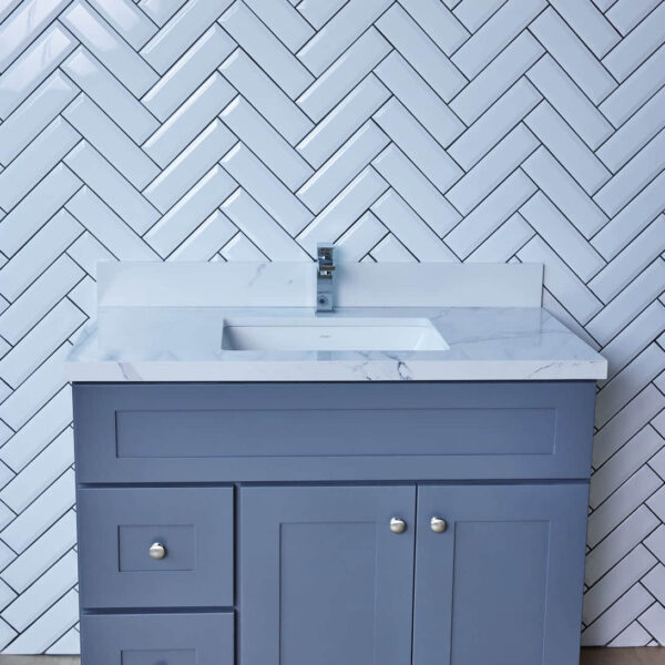Gray bathroom vanity with marble countertop against herringbone tile wall.