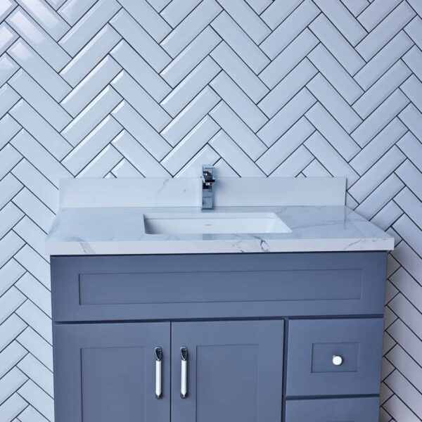 Gray bathroom vanity with marble countertop and herringbone tile backsplash.