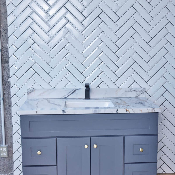 Gray bathroom vanity with marble countertop and herringbone tile backsplash.