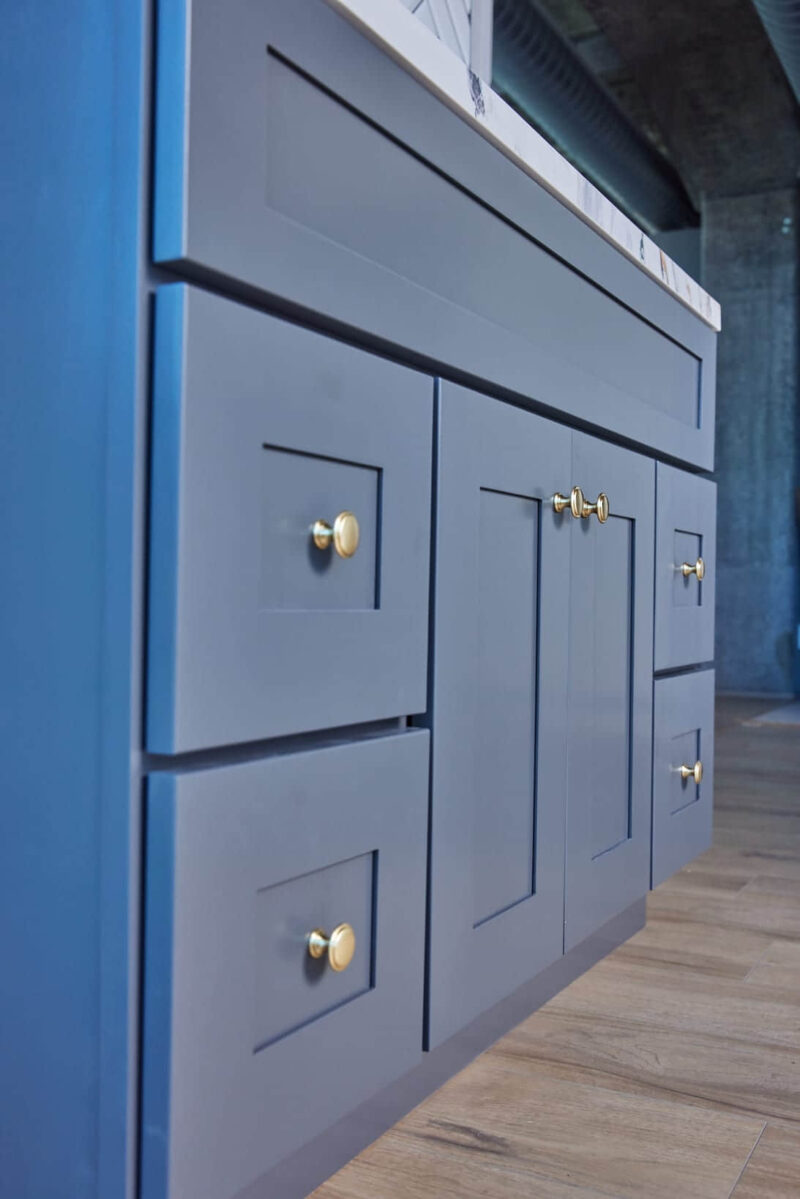 Blue kitchen cabinets with gold handles on wooden floor.
