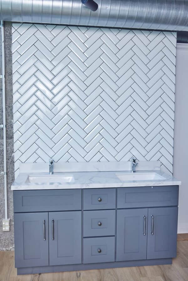 Modern kitchen with herringbone tile backsplash and gray cabinets.