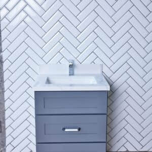 Gray bathroom vanity against white herringbone tile wall.