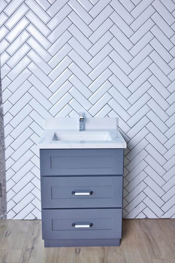 Gray bathroom vanity against white herringbone tile wall.