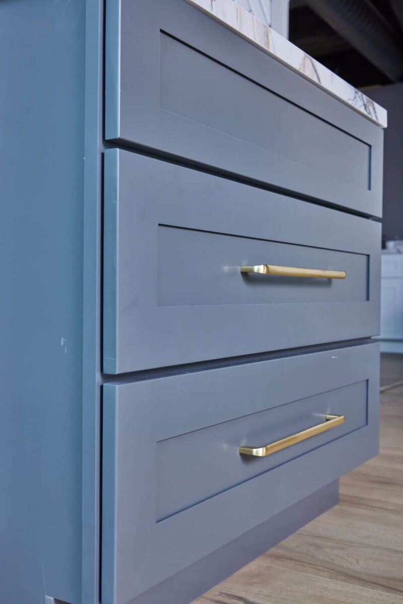 Gray bathroom vanity with marble countertop and herringbone tile backsplash.