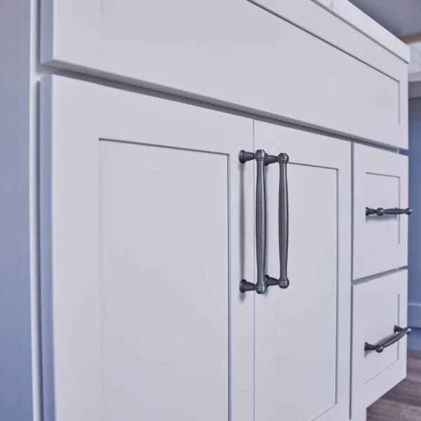 White kitchen cabinets with black handles, featuring a marble countertop.