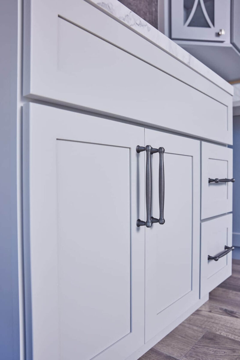 White kitchen cabinets with black handles, featuring a marble countertop.