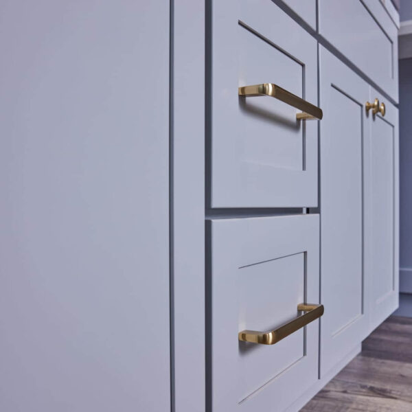 White kitchen cabinets with gold handles on wooden floor.