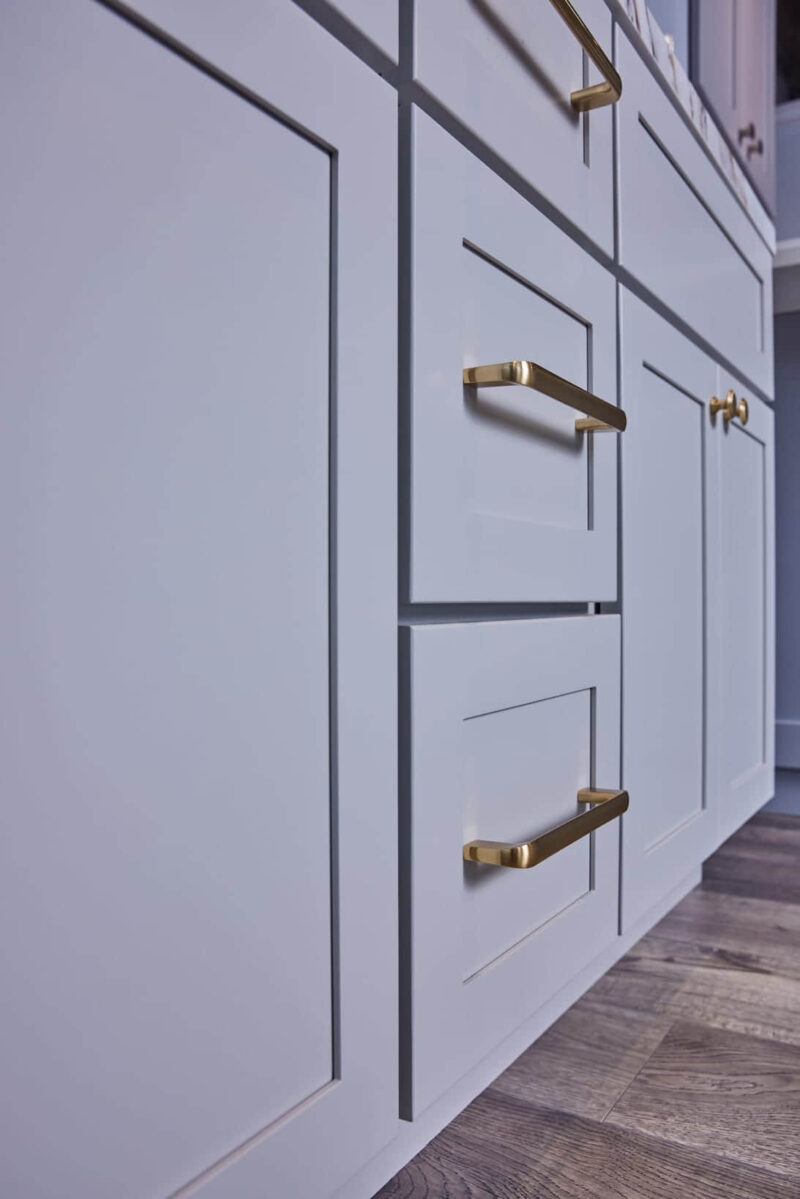 White kitchen cabinets with gold handles on wooden floor.