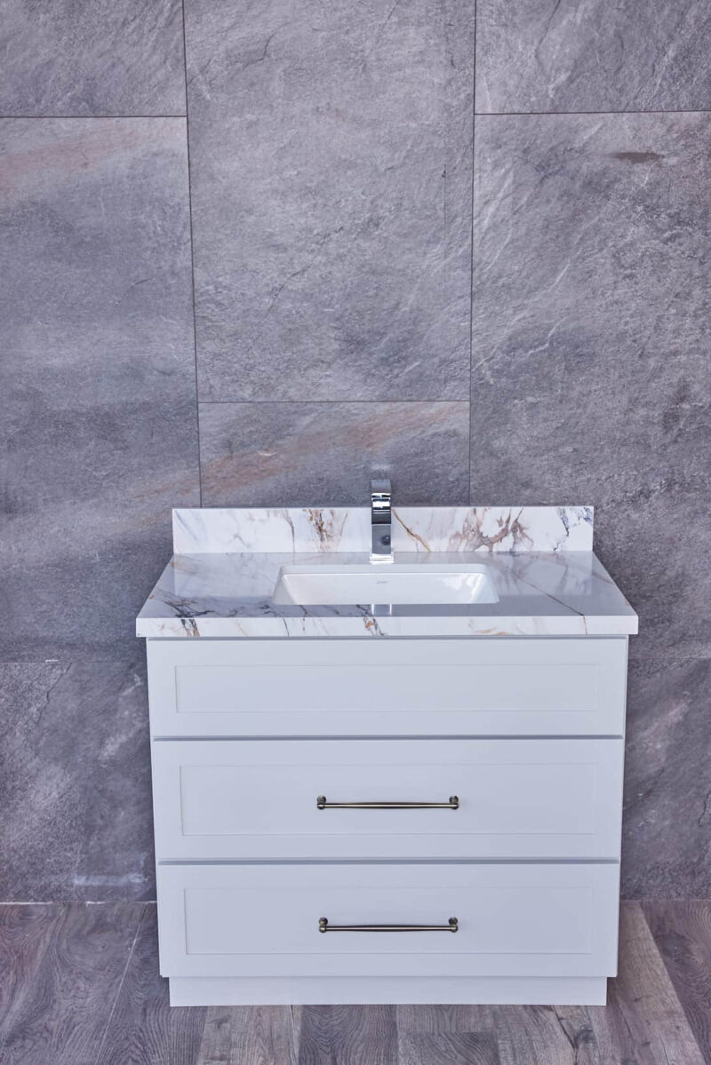 White bathroom vanity with marble countertop against gray tiled wall.