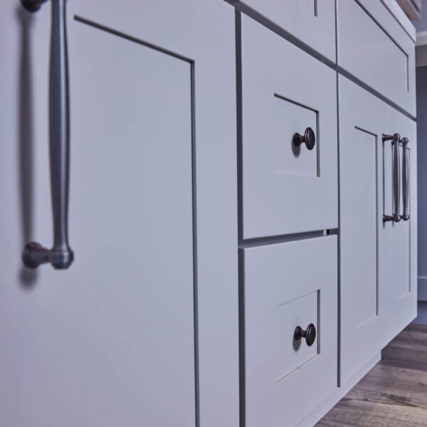 White kitchen cabinets with black handles on wooden floor.
