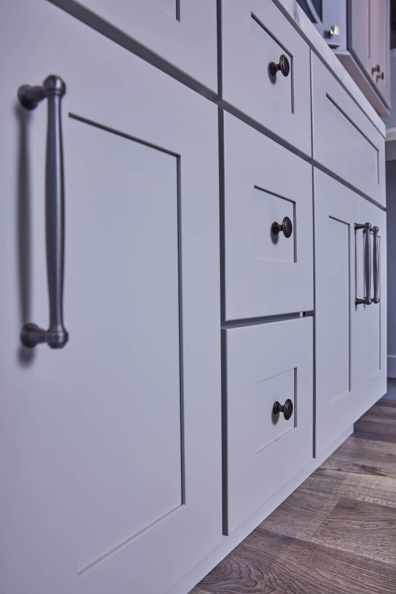 White kitchen cabinets with black handles on wooden floor.