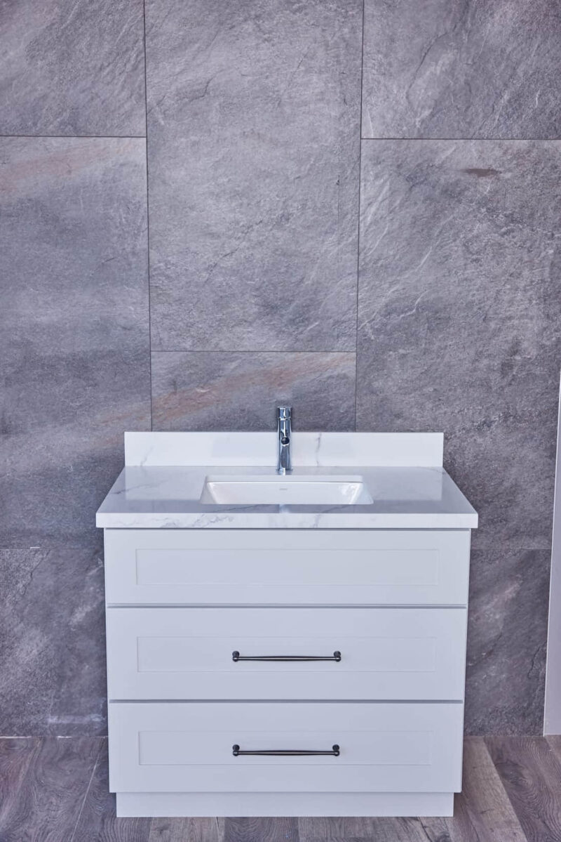 White bathroom vanity with marble countertop against gray tiled wall.
