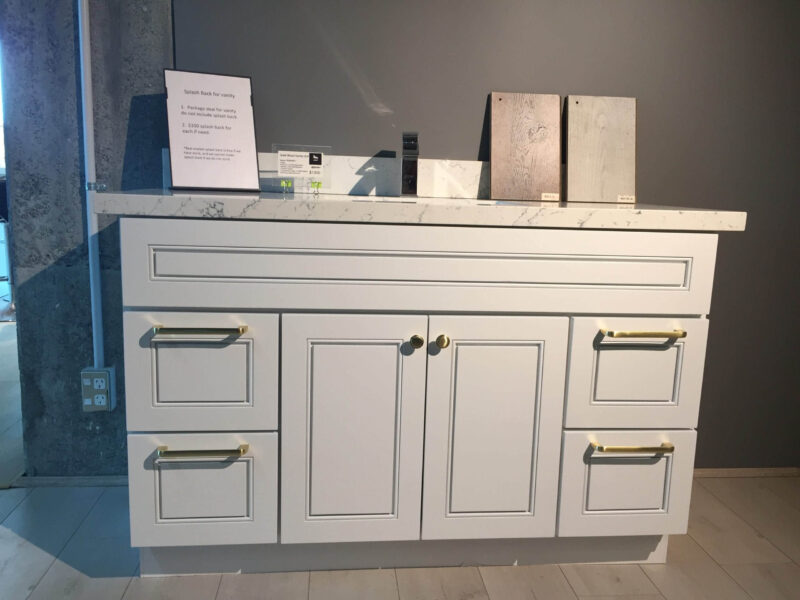 White kitchen cabinet with marble countertop and brass handles.