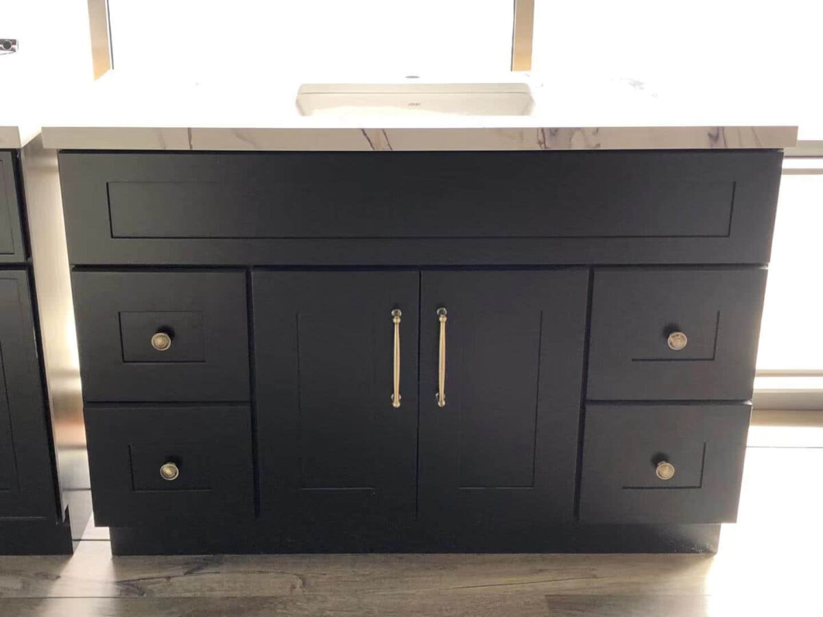 Black kitchen cabinet with marble countertop and brass handles.