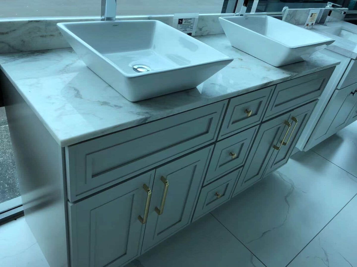 Light grey kitchen cabinet with marble countertop and two sinks.