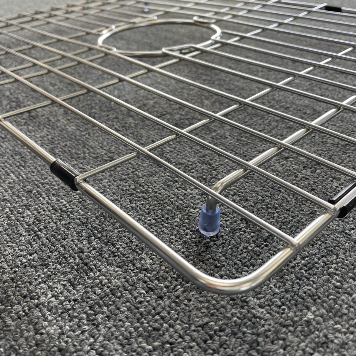 Stainless steel sink grid on textured carpet.