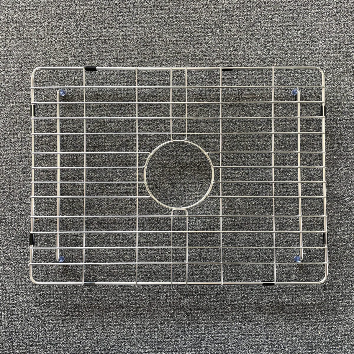 Stainless steel sink grid on a textured surface.