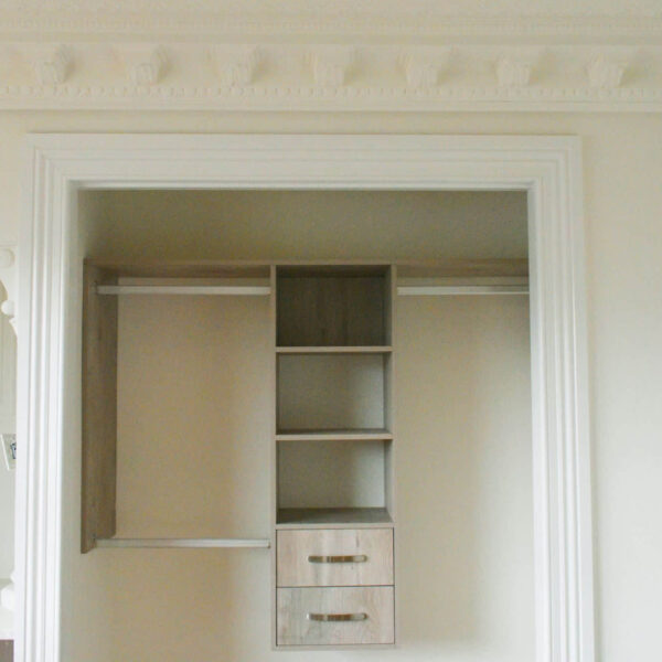 Elegant open wardrobe with shelves and drawers, featuring ornate ceiling moldings.