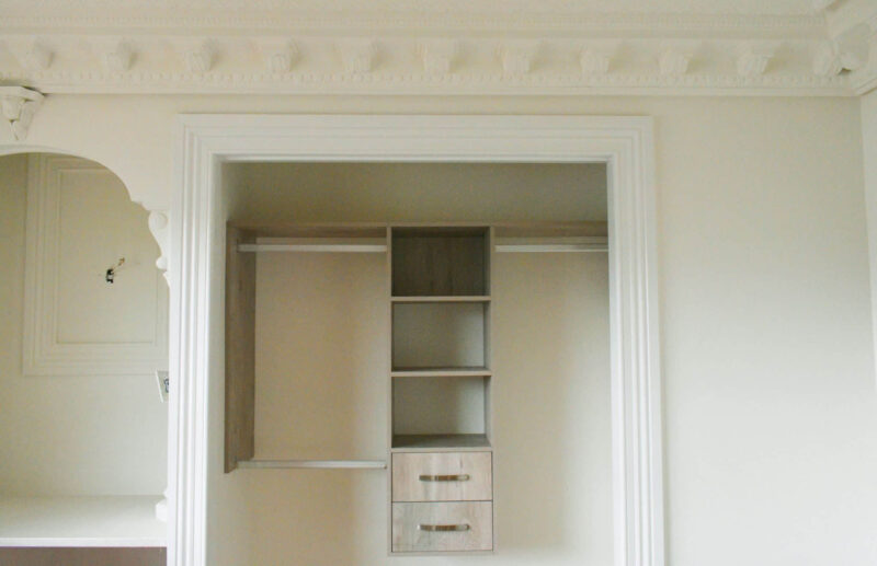 Elegant open wardrobe with shelves and drawers, featuring ornate ceiling moldings.