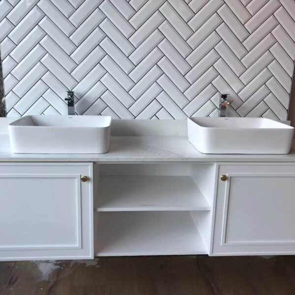 White double sink vanity with herringbone tile backsplash.