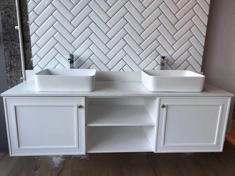 White double sink vanity with herringbone tile backsplash.