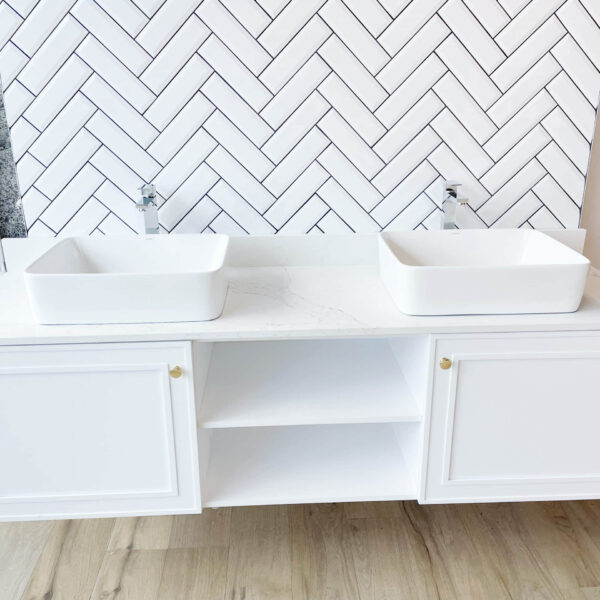 Wooden bathroom vanity with marble countertop and herringbone tile backsplash.