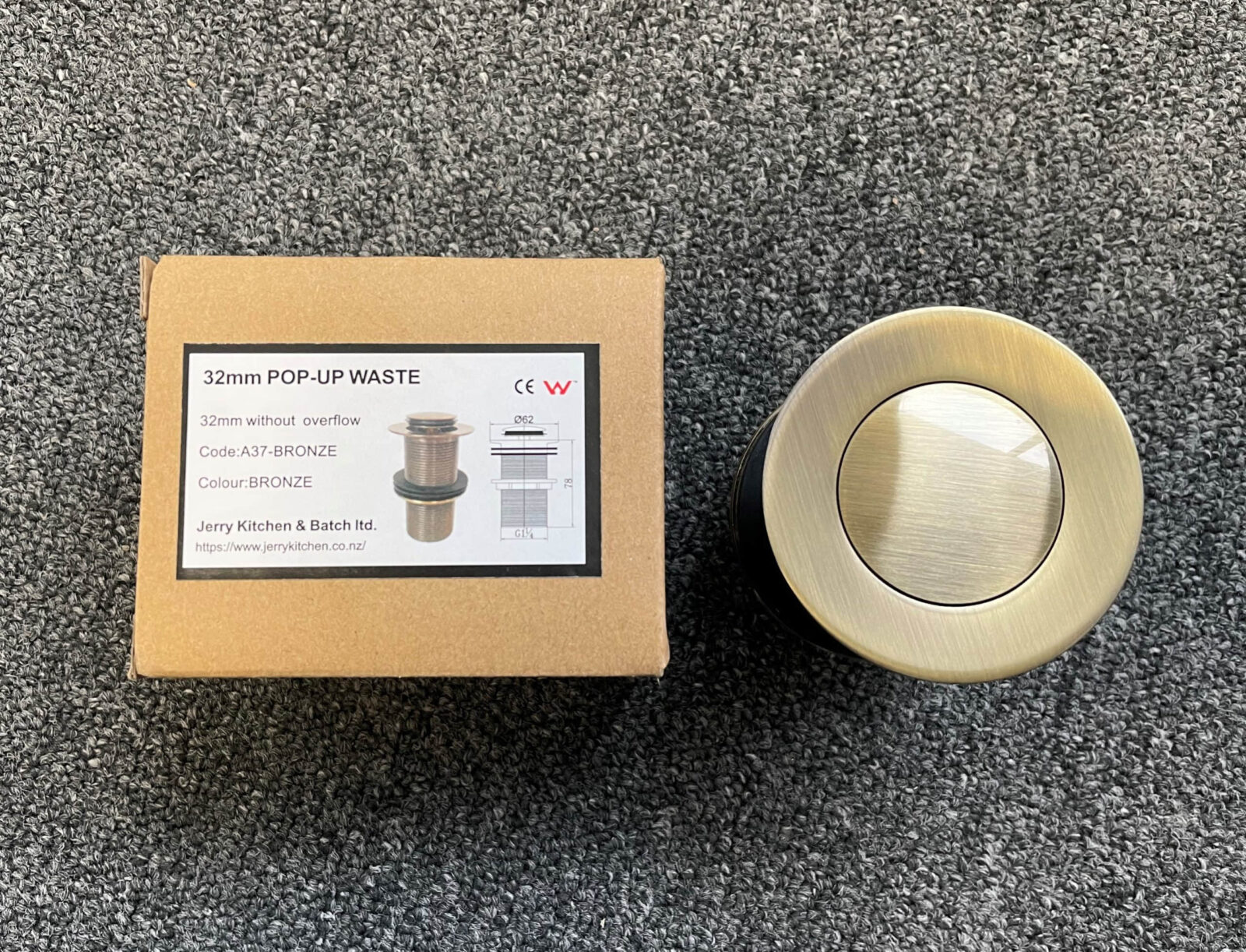 Bronze 32mm pop-up waste with packaging on carpet.