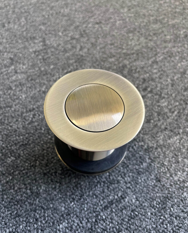 Bronze pop-up waste plug on gray surface, top view.