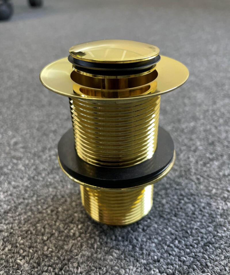 Gold pop-up waste drain on textured surface.