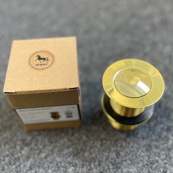 Gold pop-up waste drain with packaging on gray surface.