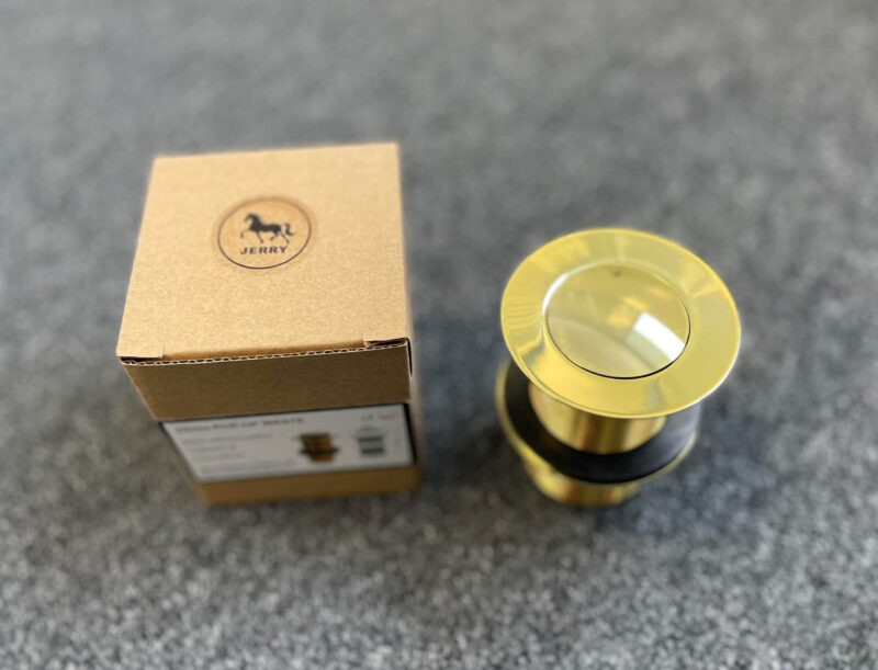 Gold pop-up waste drain with packaging on gray surface.
