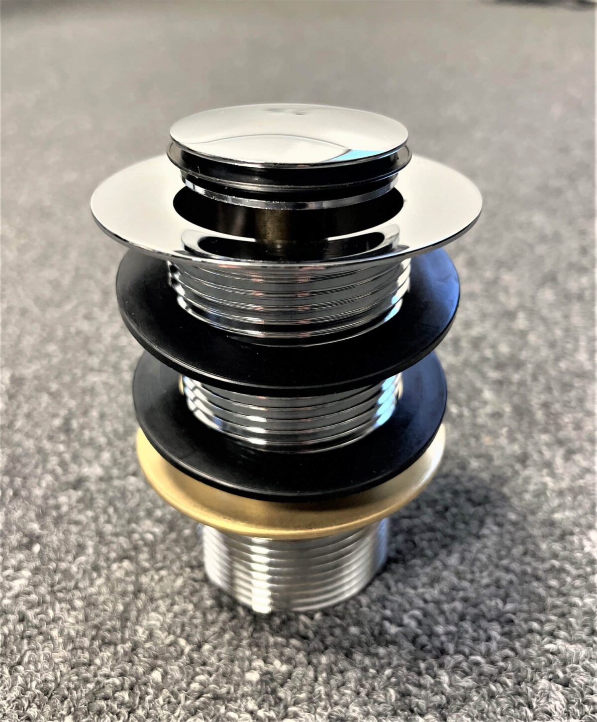 Chrome pop-up waste without overflow on carpeted surface.