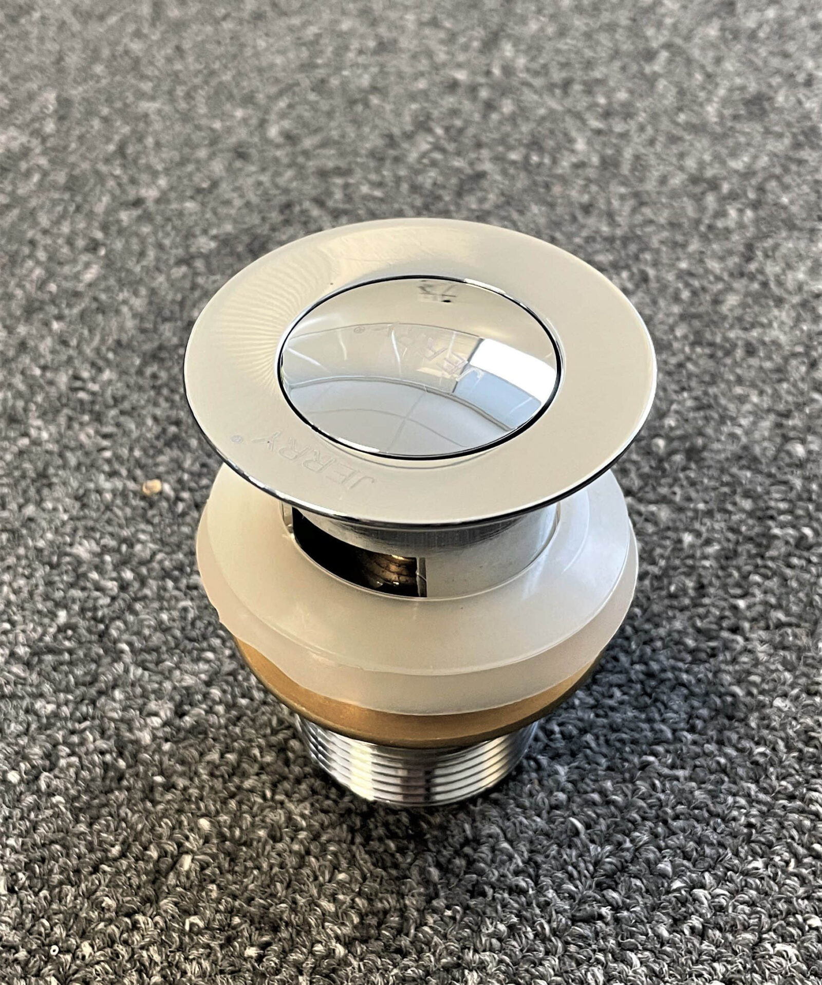 Chrome solid brass pop-up waste with overflow on gray surface.