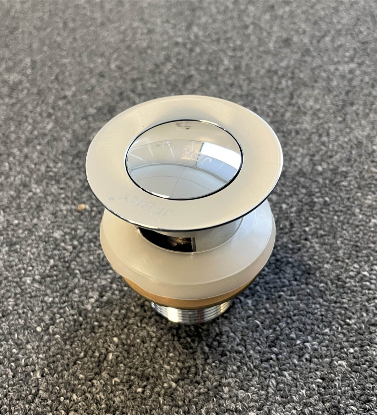 Chrome solid brass pop-up waste with overflow on gray surface.