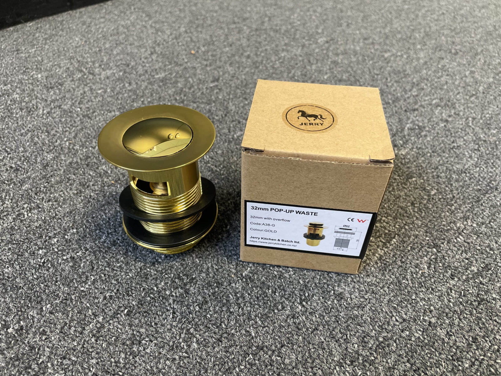 Gold pop-up waste with overflow next to labeled box on carpet.