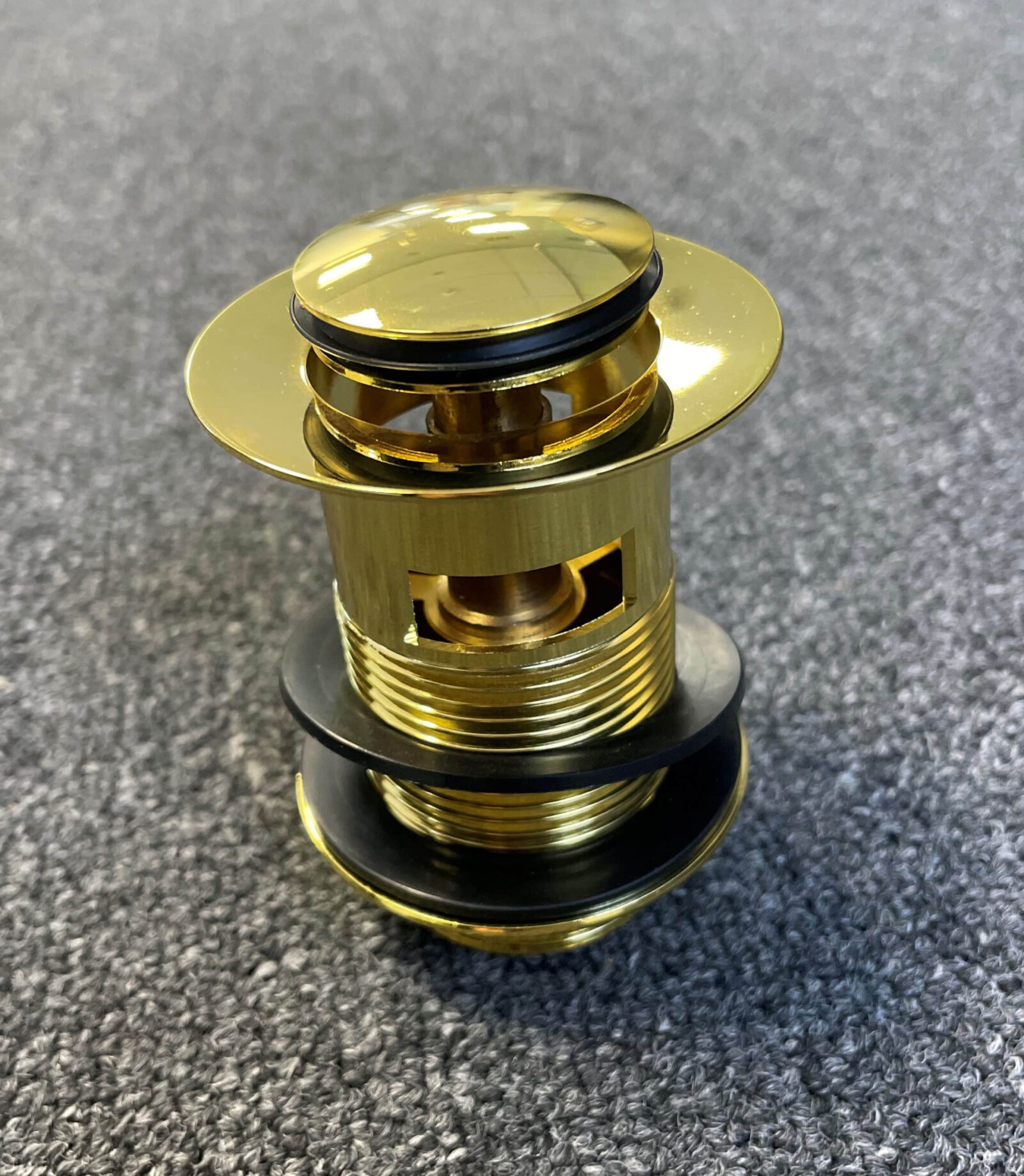 Gold pop-up waste with overflow on gray surface.