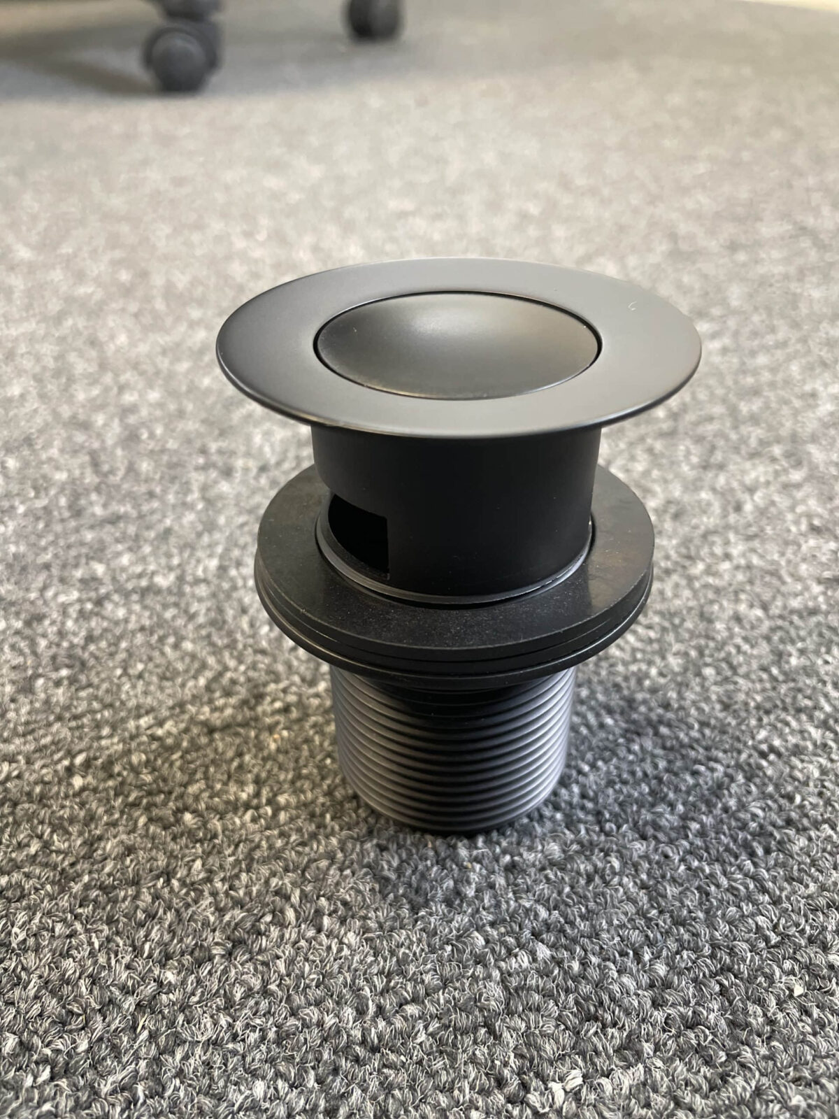 Matt black pop-up waste with overflow on gray surface.