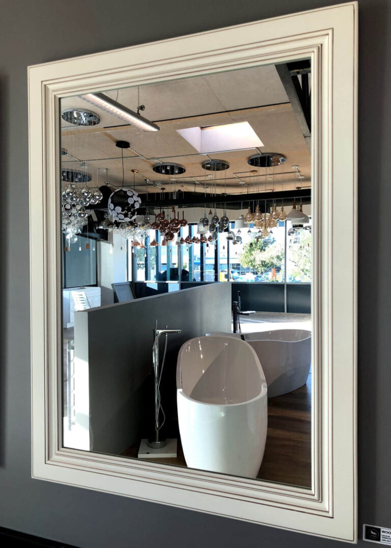 Framed mirror reflecting modern bathroom showroom with bathtubs and lighting fixtures.
