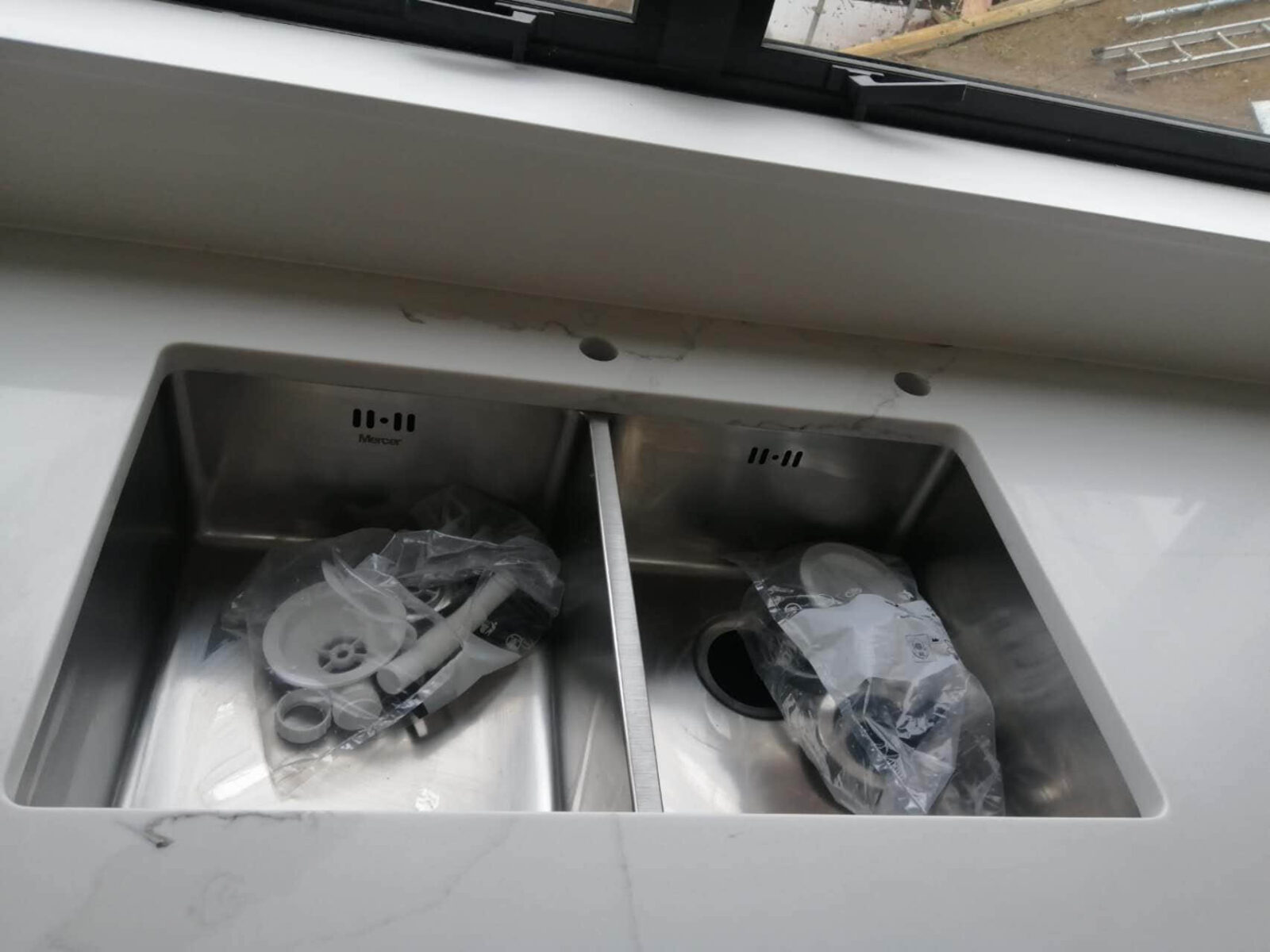 Double kitchen sink with plumbing parts on a marble countertop.