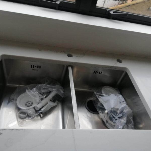 Double kitchen sink with plumbing parts on a marble countertop.