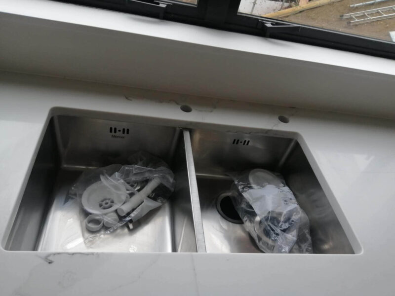 Double kitchen sink with plumbing parts on a marble countertop.