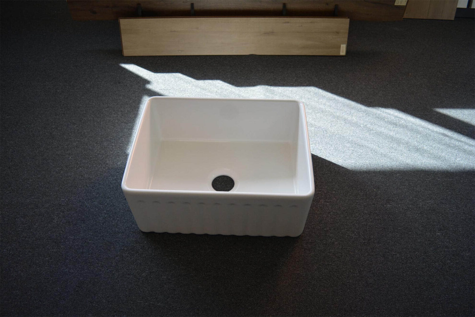 White ceramic kitchen sink on dark carpeted floor.